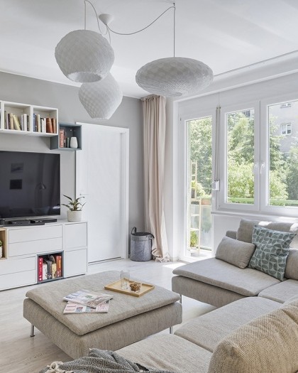 A cozy living room featuring a couch, coffee table, and bookshelves, illuminated by a stylish white C pendant light.